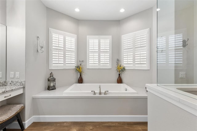 bathroom with a garden tub, recessed lighting, and vanity