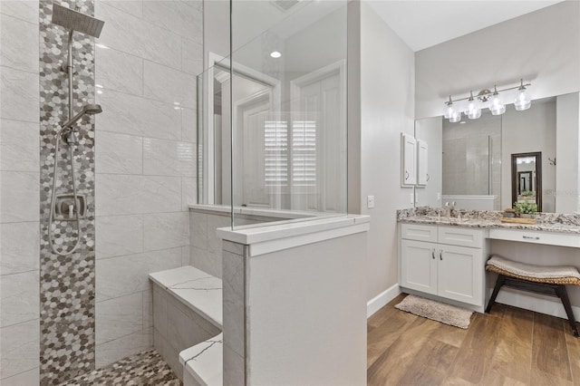 bathroom featuring a walk in shower, vanity, baseboards, and wood finished floors