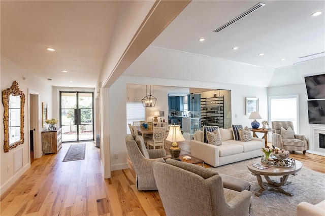 living area with visible vents, plenty of natural light, a fireplace with raised hearth, and light wood finished floors