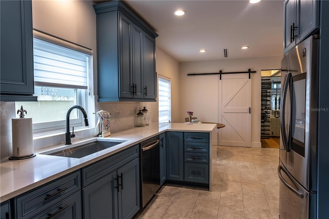 kitchen with light countertops, a barn door, appliances with stainless steel finishes, a peninsula, and a sink