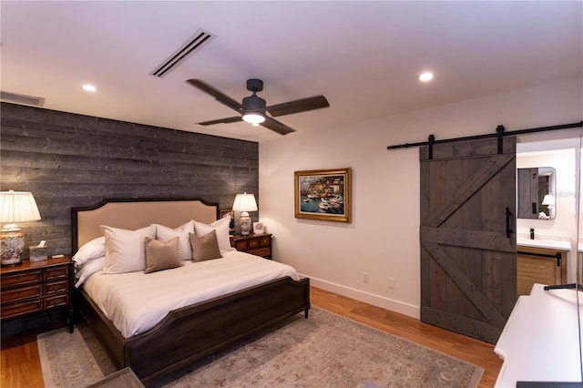 bedroom featuring recessed lighting, visible vents, a barn door, and wood finished floors