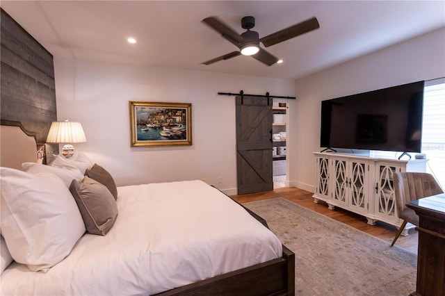 bedroom with wood finished floors, baseboards, recessed lighting, ceiling fan, and a barn door