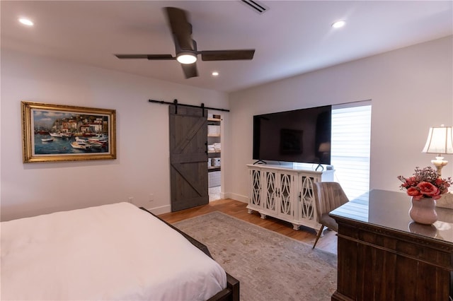 bedroom featuring recessed lighting, a barn door, visible vents, and wood finished floors