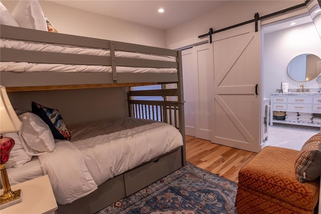 bedroom with recessed lighting, light wood-style flooring, a barn door, and a sink