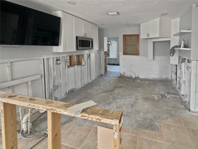 kitchen with open shelves, stainless steel microwave, and white cabinets