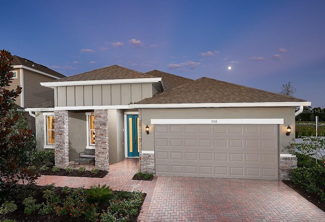 view of front of home featuring a shingled roof, stone siding, an attached garage, decorative driveway, and stucco siding