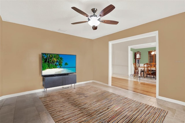 unfurnished living room with light tile patterned floors, visible vents, a ceiling fan, and baseboards