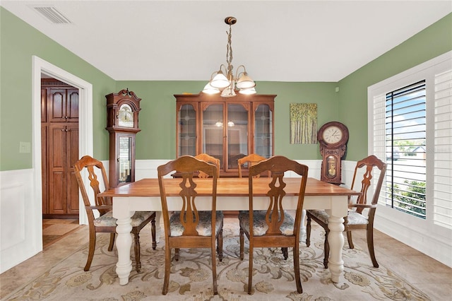 dining area with a wainscoted wall, an inviting chandelier, light tile patterned floors, and visible vents