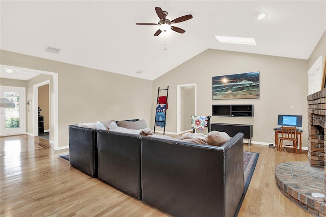 living area with visible vents, vaulted ceiling with skylight, ceiling fan, light wood-style floors, and a brick fireplace