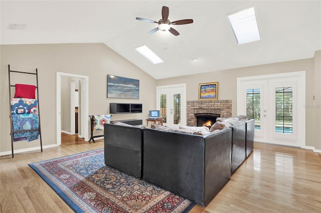 living area with a fireplace, vaulted ceiling with skylight, french doors, and light wood finished floors