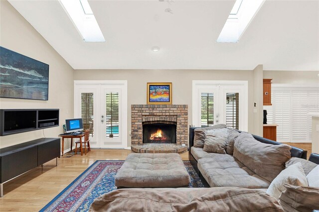 living room with light wood finished floors, vaulted ceiling with skylight, french doors, and a fireplace