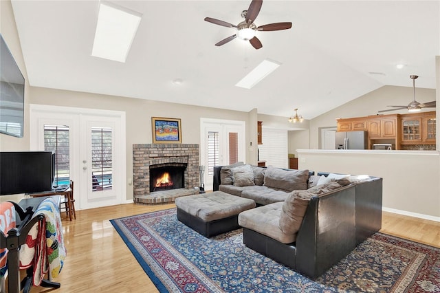 living area featuring light wood finished floors, a brick fireplace, ceiling fan, lofted ceiling with skylight, and french doors