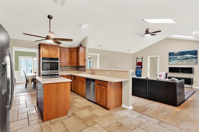 kitchen featuring stone tile floors, a peninsula, a sink, stainless steel appliances, and open floor plan