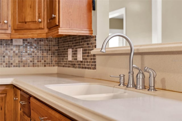 room details featuring decorative backsplash, brown cabinets, light countertops, and a sink