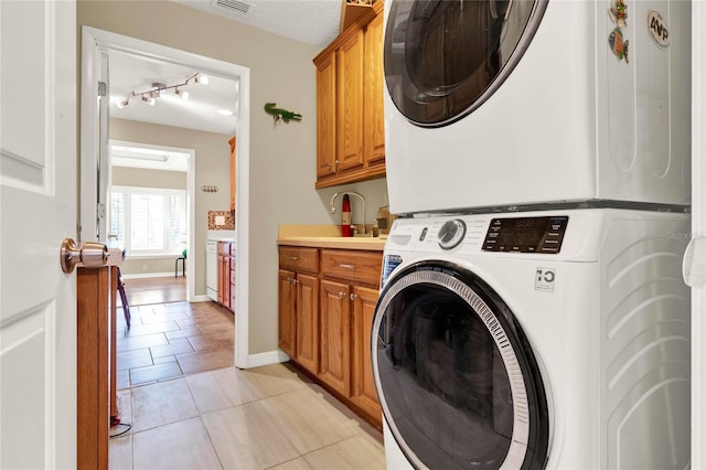 washroom with visible vents, baseboards, stacked washer and clothes dryer, light tile patterned flooring, and cabinet space