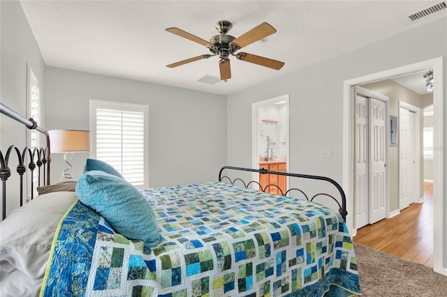 bedroom with visible vents, baseboards, wood finished floors, a textured ceiling, and a ceiling fan