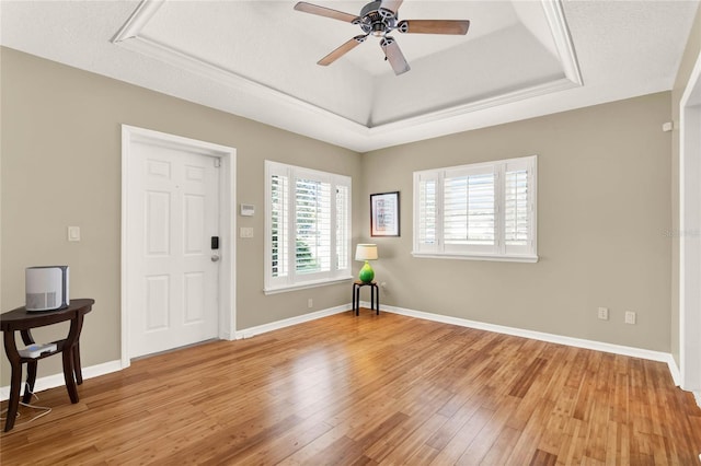 unfurnished room with light wood-type flooring, a tray ceiling, and baseboards