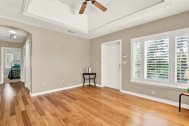 interior space with light wood-style floors, a tray ceiling, visible vents, and arched walkways