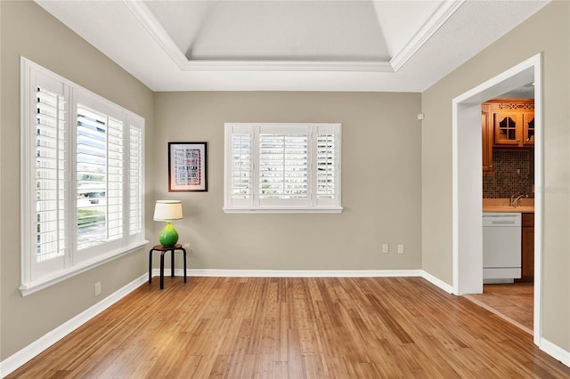 spare room with a tray ceiling, baseboards, light wood-style flooring, and ornamental molding