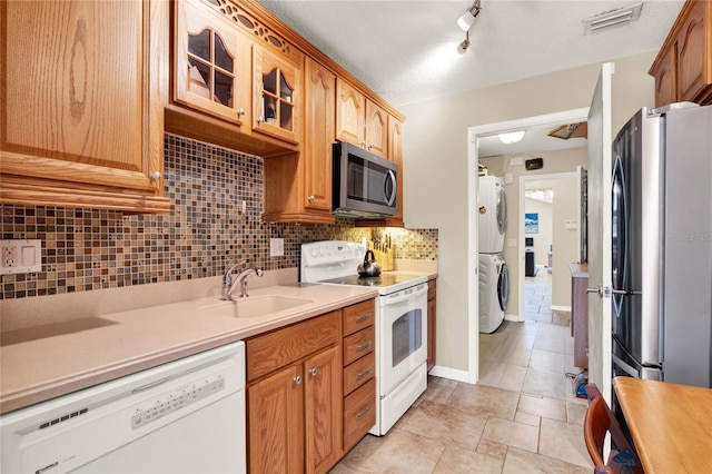 kitchen featuring visible vents, a sink, stainless steel appliances, light countertops, and stacked washer / drying machine