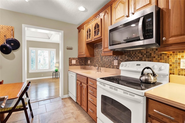 kitchen featuring white appliances, a sink, decorative backsplash, light countertops, and glass insert cabinets