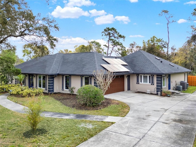 single story home with stucco siding, roof mounted solar panels, a garage, and a front lawn