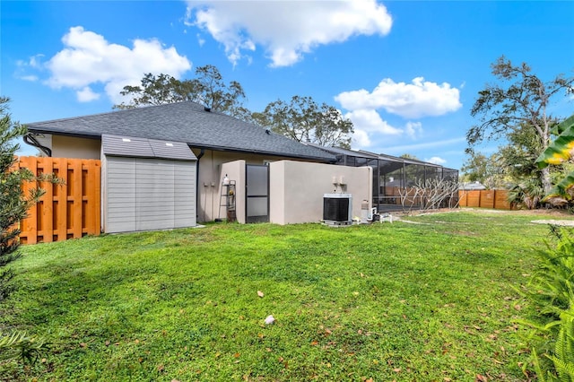 rear view of property with a lanai, central air condition unit, a lawn, a fenced backyard, and an outbuilding