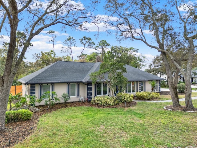 ranch-style house featuring stucco siding, roof with shingles, a front lawn, and fence