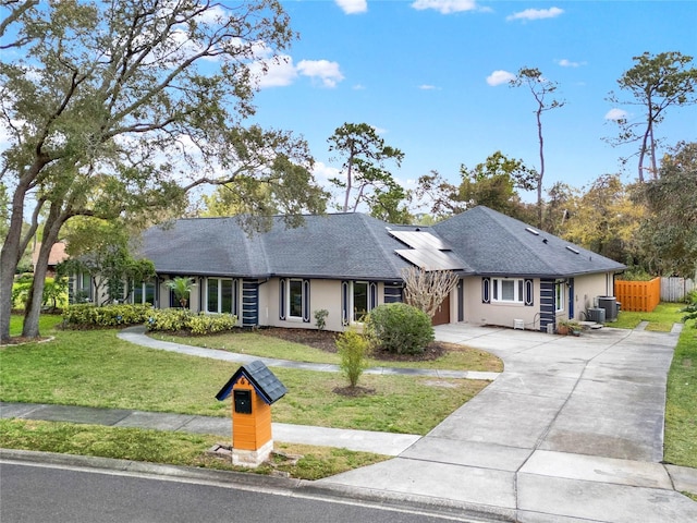 ranch-style home with driveway, roof mounted solar panels, fence, a front yard, and a shingled roof