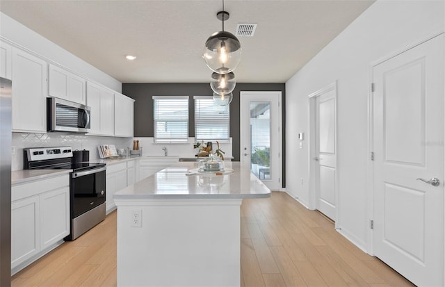 kitchen featuring light wood-style flooring, a kitchen island, white cabinets, appliances with stainless steel finishes, and decorative backsplash