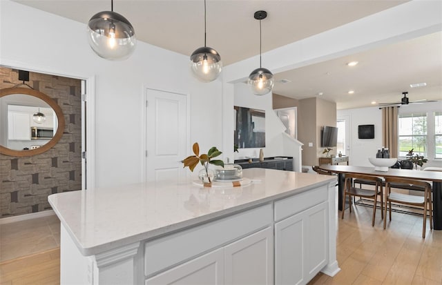 kitchen featuring open floor plan, stainless steel microwave, white cabinetry, and light wood-style floors