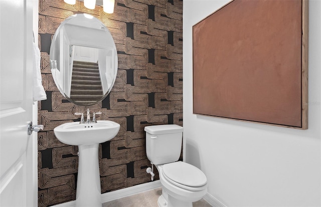 bathroom featuring toilet, wallpapered walls, and baseboards