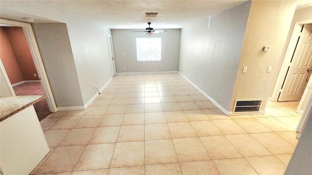 interior space with light tile patterned floors, ceiling fan, a textured wall, and visible vents