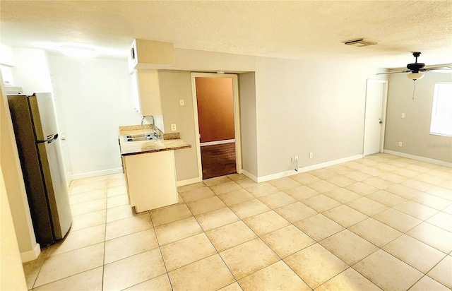 kitchen featuring light countertops, visible vents, freestanding refrigerator, a sink, and a textured ceiling