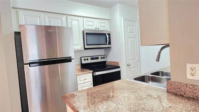 kitchen with appliances with stainless steel finishes, white cabinets, a sink, and light countertops