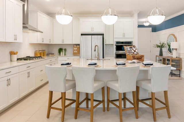 kitchen featuring wall chimney exhaust hood, appliances with stainless steel finishes, light countertops, crown molding, and a kitchen bar