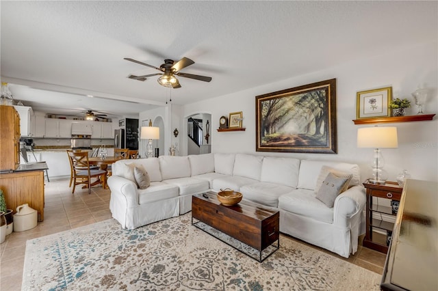 living room featuring arched walkways, visible vents, a ceiling fan, light tile patterned flooring, and a textured ceiling