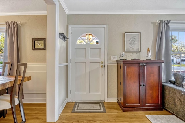 foyer with ornamental molding, a wainscoted wall, and light wood-style floors