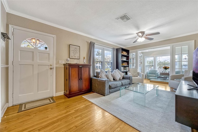 living area featuring ceiling fan, a textured ceiling, light wood-style flooring, visible vents, and ornamental molding