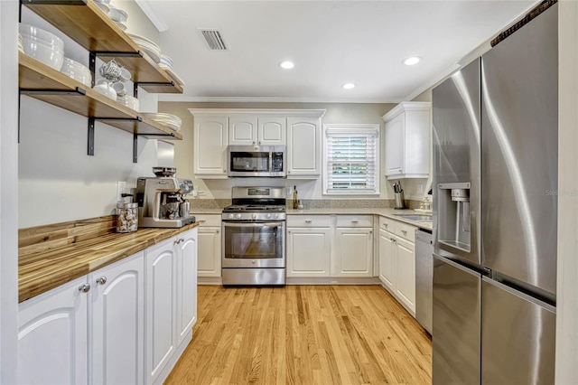 kitchen featuring light wood finished floors, open shelves, appliances with stainless steel finishes, ornamental molding, and white cabinetry