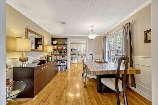 dining room featuring ornamental molding, visible vents, light wood-style flooring, and a textured ceiling