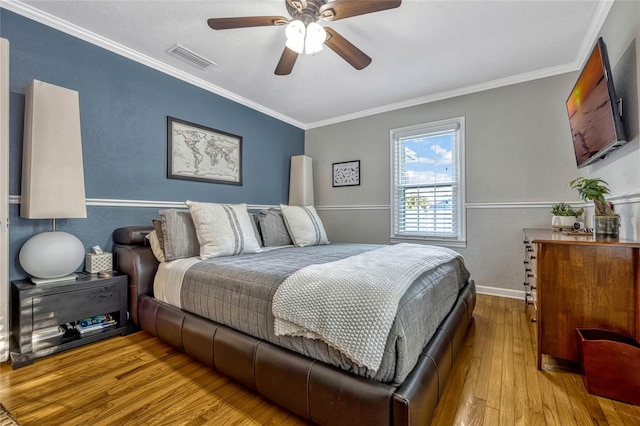 bedroom featuring ceiling fan, hardwood / wood-style flooring, visible vents, baseboards, and crown molding