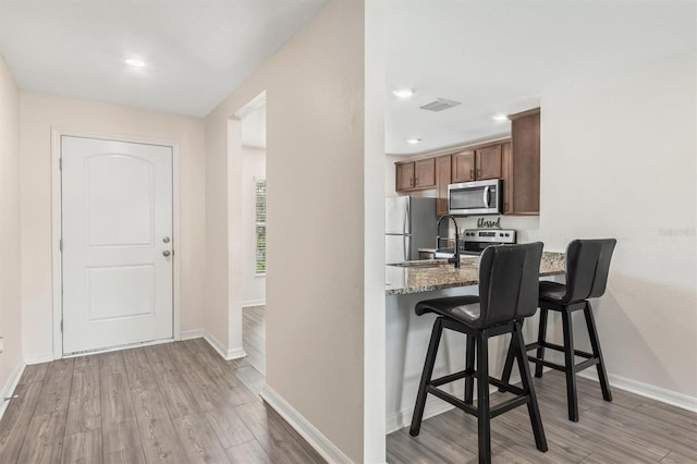 kitchen featuring light stone countertops, stainless steel appliances, a breakfast bar, light wood-style floors, and brown cabinets