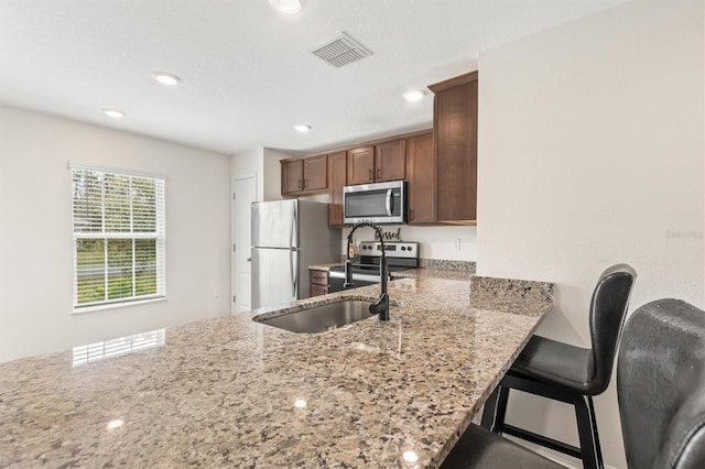 kitchen with visible vents, appliances with stainless steel finishes, a breakfast bar, light stone counters, and a peninsula