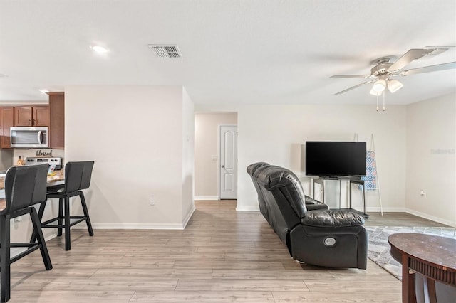 living area featuring ceiling fan, light wood-type flooring, visible vents, and baseboards