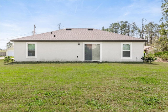 rear view of house featuring roof with shingles, a lawn, and stucco siding