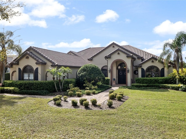 mediterranean / spanish-style house featuring stucco siding, a tiled roof, and a front yard