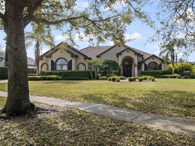 mediterranean / spanish house with a front yard, a tile roof, and stucco siding