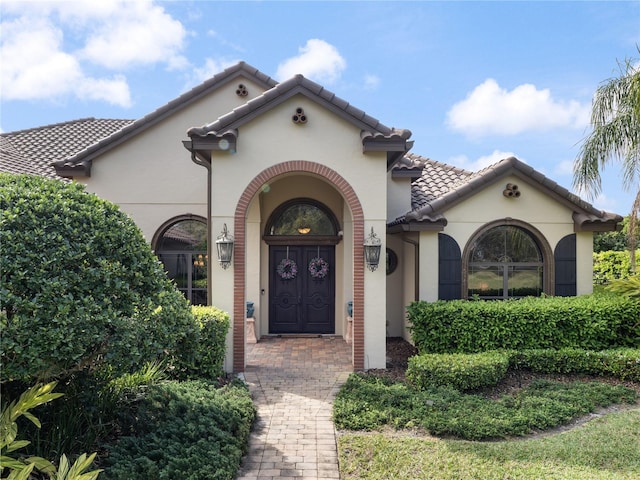 view of exterior entry with a tile roof and stucco siding