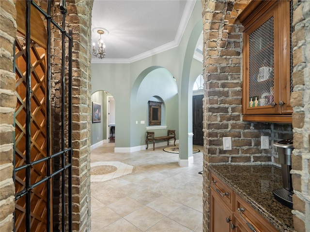 interior space featuring arched walkways, crown molding, light tile patterned floors, an inviting chandelier, and baseboards